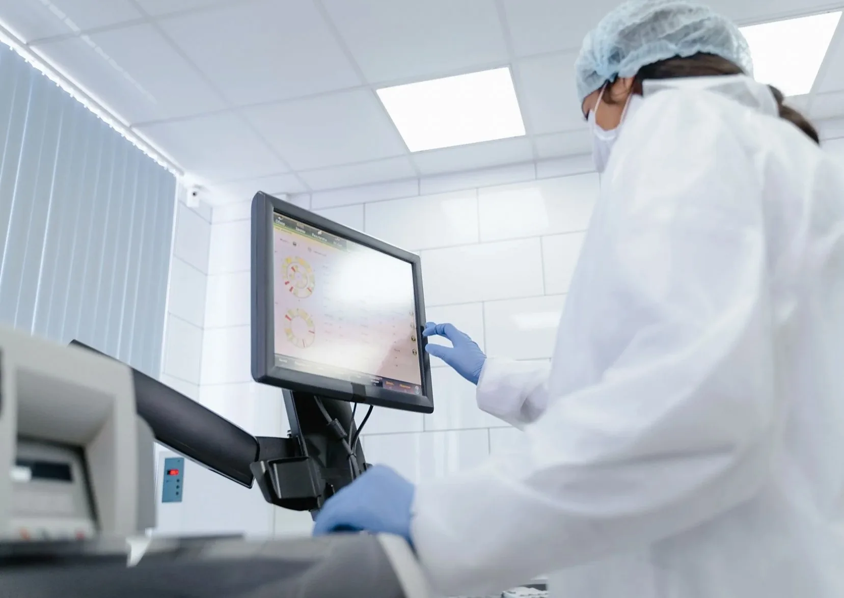 Woman in lab coat using touchscreen monitor in a modern laboratory setting.